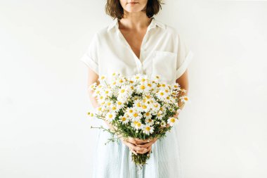 Genç ve güzel bir kadın beyaz arka planda bir buket papatya çiçeği tutuyor..