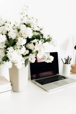 Masasında boş kopya alanı olan bir dizüstü bilgisayar. Ofis masası çalışma alanı çiçek buketi, masa lambası.