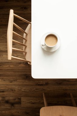 Sütlü bir fincan kahve. Tasarımcı sandalyesi ve ahşap zeminin yanında. Modern iç mimari mobilya konsepti.