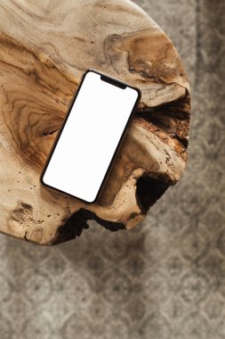 Boş ekran akıllı telefon. Saf ahşap tabure ve halının üzerinde boş bir kopya alanı var. Düz konum, sosyal medya, web sitesi, dergi için üst görünüm şablonu.