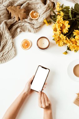 Women home office table desk with blank screen mobile phone with copy space. Yellow daisy flowers bouquet, decorations. Flat lay, top view freelance business concept for social media, magazine.