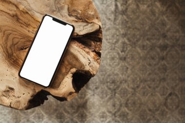 Boş ekran akıllı telefon. Saf ahşap tabure ve halının üzerinde boş bir kopya alanı var. Düz konum, sosyal medya, web sitesi, dergi için üst görünüm şablonu.