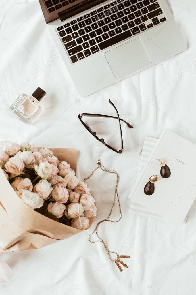 Fashion, beauty, lifestyle blogger home office workspace. Laptop, roses bouquet, female accessories, notebook on white linen. Flat lay, top view freelancer concept.