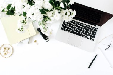 Laptop ve çiçek buketi beyaz masada. Flatlay, üst görünüm en az ofis masası arkaplanı.