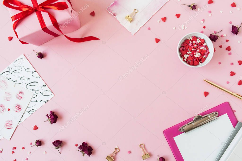 Valentine's Day composition. Blank copy space frame on pink background. Gift box, clipboard, rose buds, heart symbol confetti. Flat lay, top view.