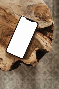 Saf ahşap tabure ve halıya boş fotokopi alanı modeliyle boş ekran cep telefonu. Düz konum, sosyal medya, web sitesi, dergi için üst görünüm şablonu.