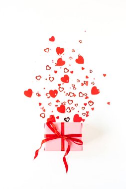 Beyaz arka planda pembe hediye kutusu ve kalp sembolü konfetisi. Flatlay, Sevgililer Günü konsepti.