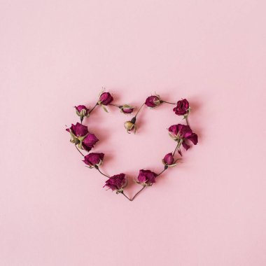 Sevgililer Günü konsepti. Pembe arka planda kurumuş gül tomurcuklarından yapılmış kalp sembolü. Düz konum, üst görünüm minimal tatil kompozisyonu.