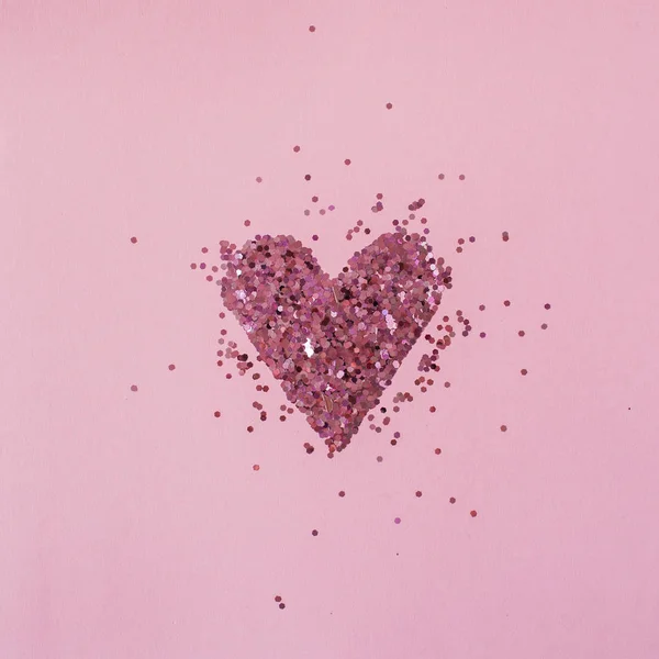バレンタインデーのコンセプト ピンクの背景に輝くコンフェッティで作られたハートシンボル フラットレイアウト 最低限の休日構成を表示 — ストック写真