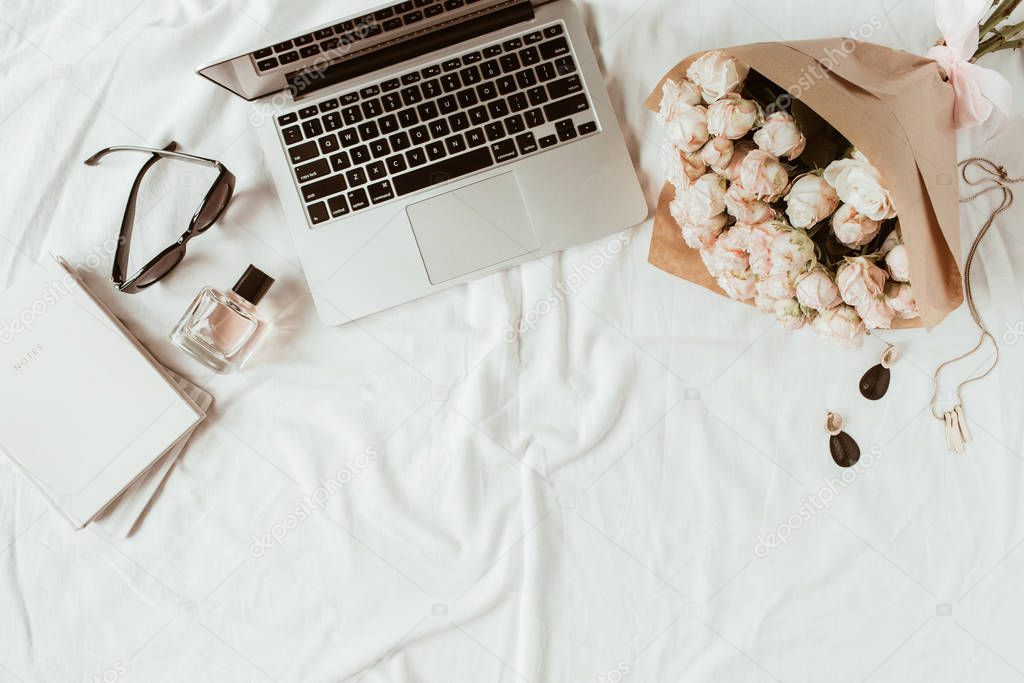 Fashion, beauty, lifestyle blogger home office workspace. Laptop, roses bouquet, women's accessories on white linen. Flat lay, top view woman work concept.