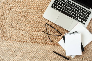 Blank sheet notebook, laptop, glasses, pen, laptop on wicker straw background. Flat lay, top view minimal home office desk workspace with copy space. Work, business, education concept.