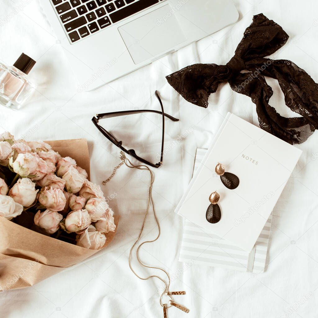Fashion, beauty, lifestyle blogger home office workspace. Laptop, roses bouquet, female accessories, notebook on white linen. Flat lay, top view freelancer concept.