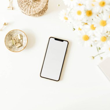 Beyaz arka planda papatya çiçeği buketi olan boş bir fotokopi masası olan cep telefonu. Düz konum, üst görünüm minimum konsept.