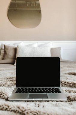 Yatakta, bej duvarın önünde yastıkları olan boş ekran laptop. Boşluk düzenleme şablonunu kopyala.