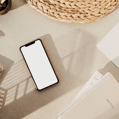 Boş ekran akıllı telefon, defterler, tahta kasede klipler, bej beton arka planda saman standı. Ofis masası çalışma alanı. İş, iş planı. Düz yatış, üst görünüm.