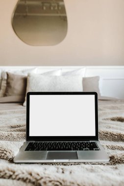 Yatakta, bej duvarın önünde yastıkları olan boş ekran laptop. Uzay modelleme şablonunu kopyala. İç tasarım günlüğü, web sitesi, sosyal medya.