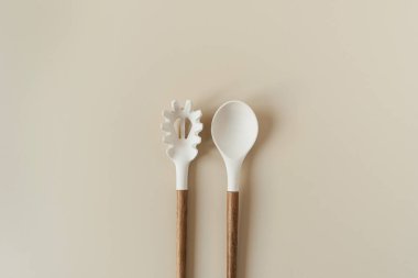 Salad serving utensils set. Spoon and fork on beige background. Minimal kitchenware concept. clipart