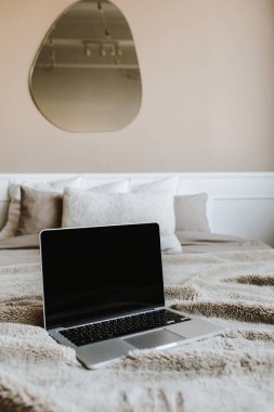 Yatakta bej duvarın önünde yastıkları olan boş ekran laptop..