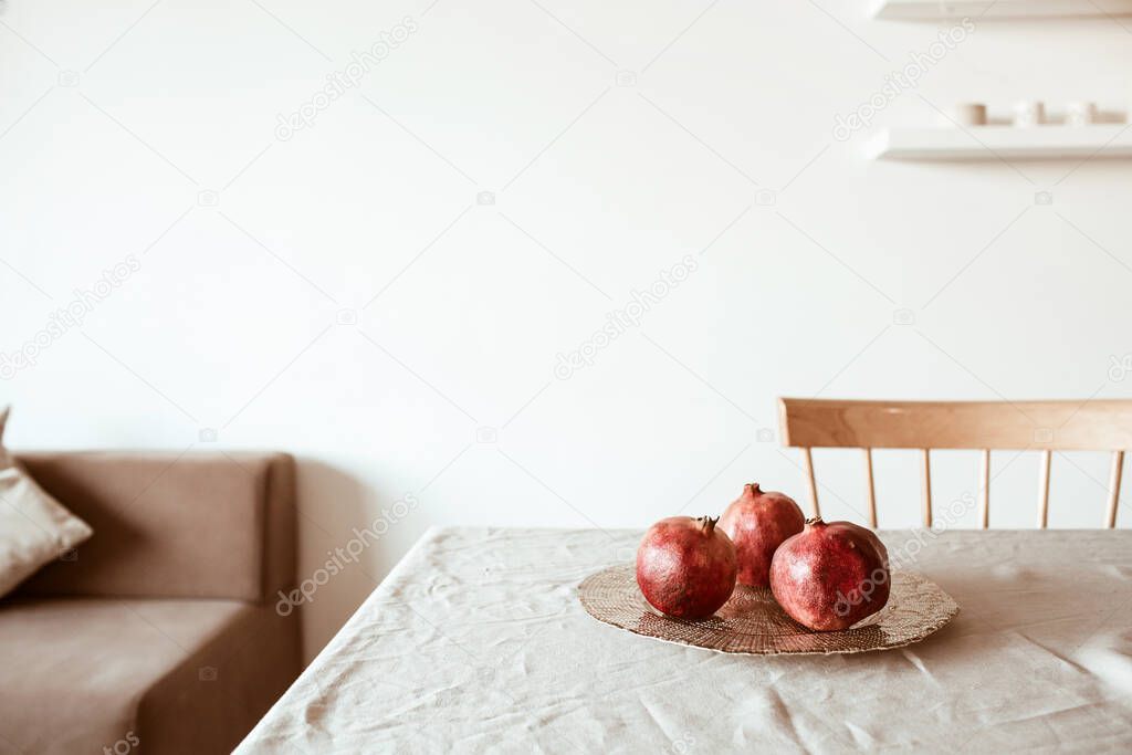 Three pomegranates on golden plate on beige table cloth.