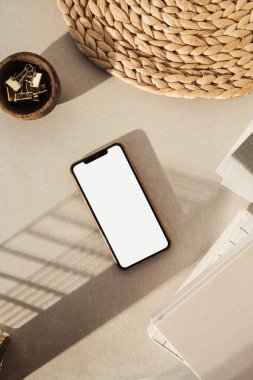 Boş ekran akıllı telefon, defterler, tahta kasede klipler, bej beton arka planda saman standı. Ofis masası çalışma alanı. İş, iş planı. Düz yatış, üst görünüm.