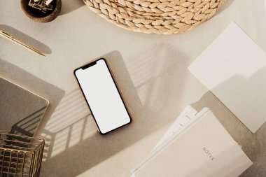 Boş ekran akıllı telefon, defterler, tahta kasede klipler, bej beton arka planda saman standı. Ofis masası çalışma alanı. İş, iş planı. Düz yatış, üst görünüm.