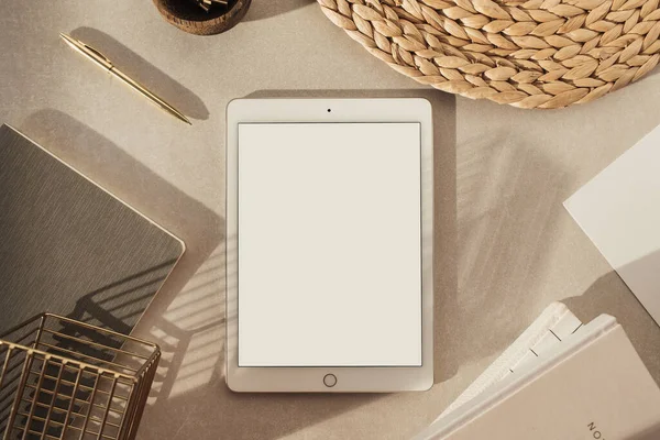 Flatlay of blank screen tablet, notebooks, clips in wooden bowl, straw stand on beige concrete background. Home office desk workspace. Business, work template. Flat lay, top view.