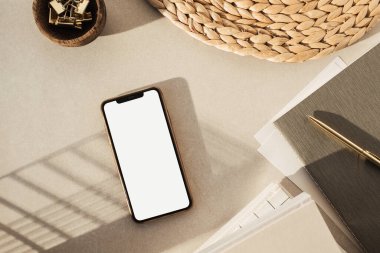 Boş ekran akıllı telefon düzlüğü, defterler, tahta kasede klipler, bej beton arka planda saman standı. Ofis masası çalışma alanı. İş, iş planı. Düz yatış, üst görünüm.
