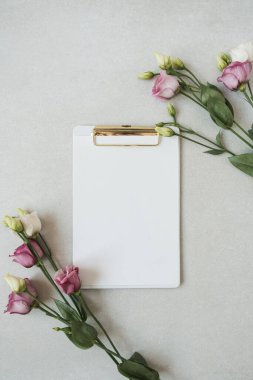 Sahte kopya alanı olan boş kağıt yaprak bloknotu, tarafsız gri arka planda güller. Düz konum, üst görünüm minimal iş şablonu