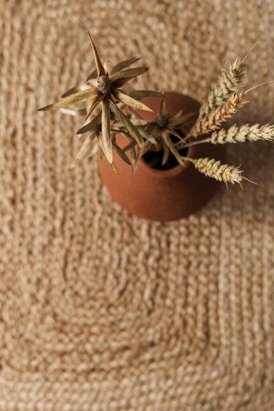 Сухой ржаной хлеб, стебли пшеницы в красном глиняном горшке на соломенном фоне. Минимальное оформление интерьера.