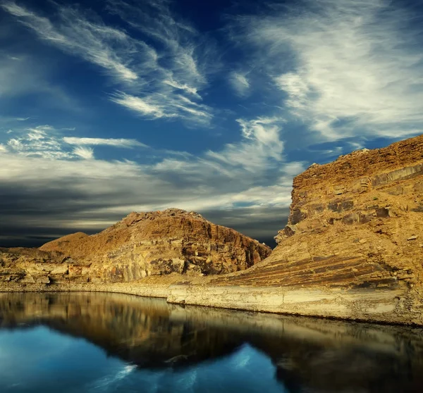 limestone cliff between cloudy sky and mirror-like surface