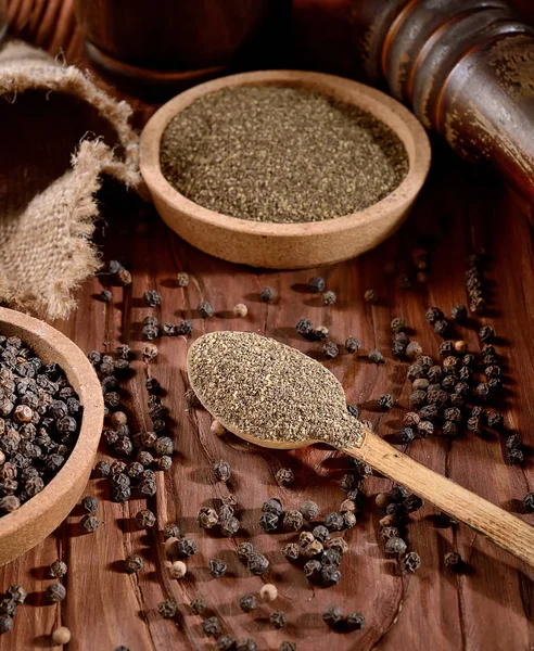 black ground pepper in spoon with grains on wooden background, rustic style