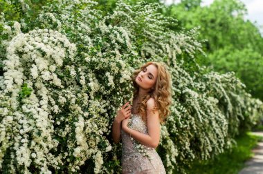 Çiçekli çalılar ve ağaçlar gülümseyen güzel arasında orta bir bahar akşam kokteyl elbise kız