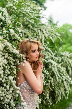 Çiçekli çalılar ve ağaçlar gülümseyen güzel arasında orta bir bahar akşam kokteyl elbise kız