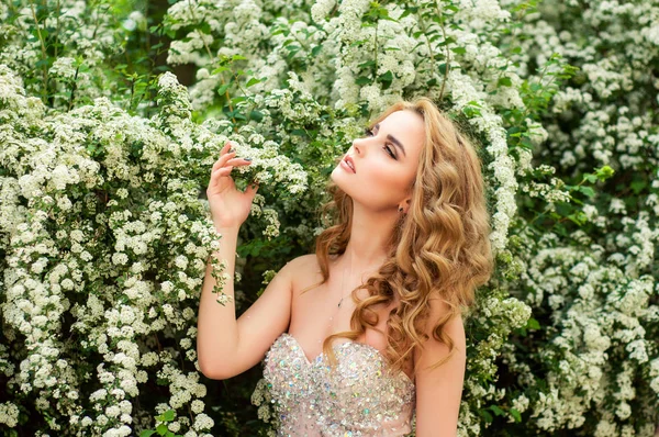 Girl in evening cocktail dress on a spring in the middle among flowering bushes and trees beautiful smiling — Stock Photo, Image