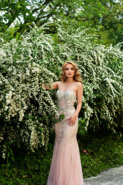 Beautiful young girl with make-up and in her dress has a good figure and looks great against the background of blooming trees in the park