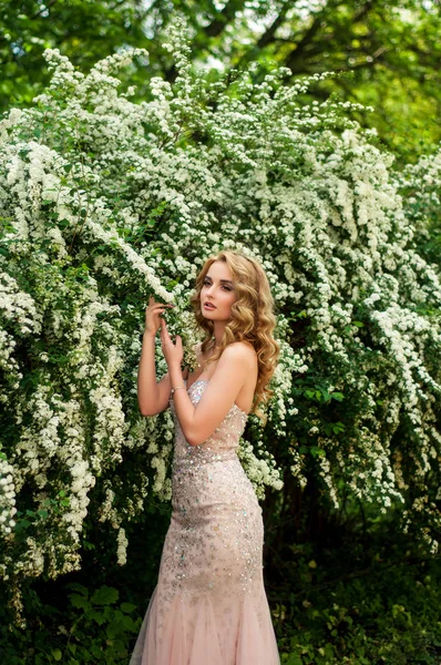 Menina em vestido de cocktail à noite em uma primavera no meio entre arbustos floridos e árvores belo sorriso — Fotografia de Stock