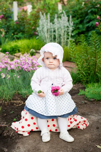 Flicka 8 månader gamla europeiska ukrainska lite baby på en promenad i trädgården lastrummen en blomma och jordgubbar i hennes händer — Stockfoto