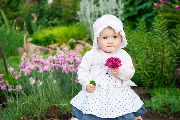 Flicka 8 månader gamla europeiska ukrainska lite baby på en promenad i trädgården lastrummen en blomma och jordgubbar i hennes händer — Stockfoto