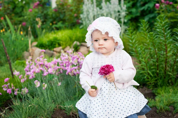 Flicka 8 månader gamla europeiska ukrainska lite baby på en promenad i trädgården lastrummen en blomma och jordgubbar i hennes händer — Stockfoto