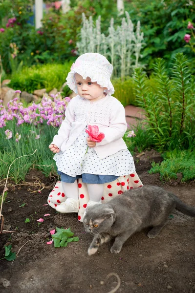 Ragazza 8 mesi piccolo bambino ucraino europeo su una passeggiata in giardino tiene un fiore e fragole nelle sue mani — Foto Stock