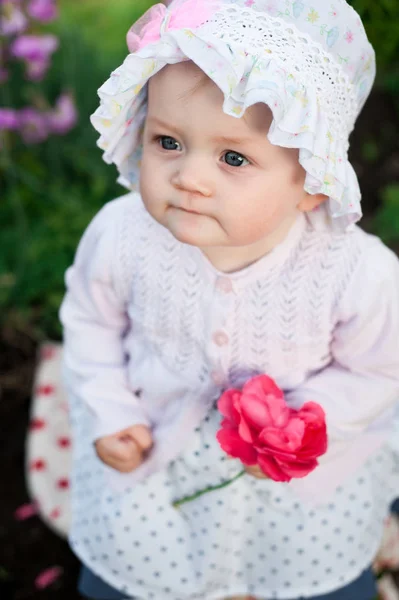 Chica de 8 meses de edad bebé ucraniano europeo en un paseo por el jardín tiene una flor y fresas en sus manos —  Fotos de Stock