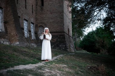 Açık havada mimari eserlerin yanında beyaz elbiseli sarışın bir kız.