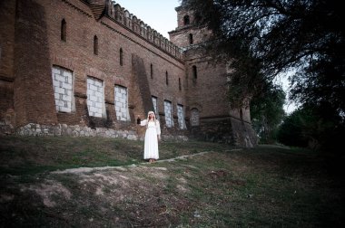 Açık havada mimari eserlerin yanında beyaz elbiseli sarışın bir kız.