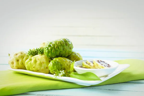 Noni fruta en el plato y noni rebanada en tela a cuadros verde . — Foto de Stock