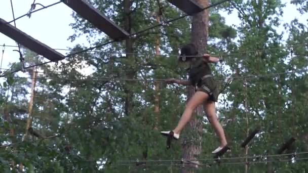 Jeune grimpeur marche par pendentif pont en rondins sur haut parcours de cordes — Video