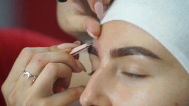 Genç bir kadın kaşlarını cımbızla koparma.