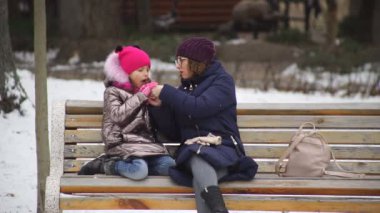 Anne ve kızı açık hava kafede bir bankta otururken eğleniyorlar. Eğlenceli bir tatilden gülümsemeler ve duygular.