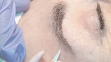 Kaş güzellik salonunda, üstat kaşlarla ilgilenir. Kadın kaşlarının tasarımı ve boyaması ve kaplaması. Renk eşleşmesi. Kozmetik bir araçla düzeltme.