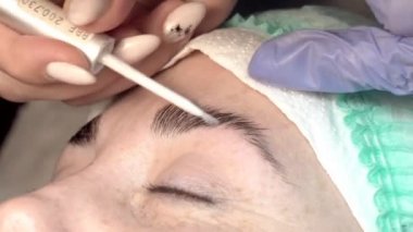 Kaş güzellik salonunda, üstat kaşlarla ilgilenir. Kadın kaşlarının tasarımı ve boyaması ve kaplaması. Renk eşleşmesi. Kozmetik bir araçla düzeltme.