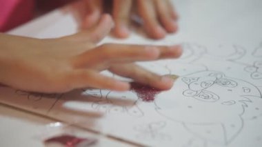 Parlak pudrayla çocuk resimleri yapar. Çocuk kağıt çizimlerini parlak tozla boyuyor, yapıştırıcıya dayanarak küçük parıltıları ovuyor. Çocukların yaratıcılığını geliştirir.